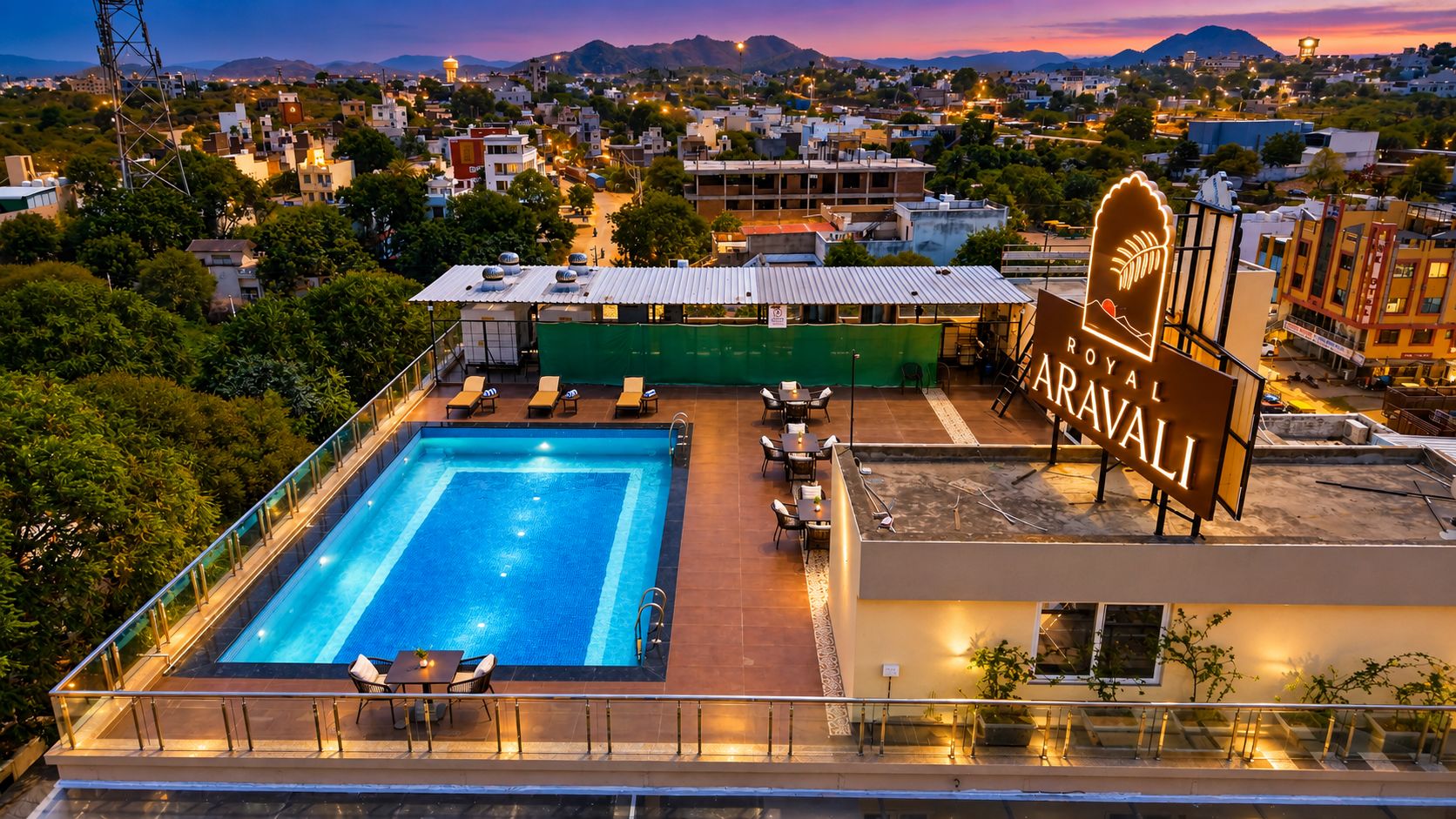 A rooftop swimming pool with lounge chairs and a sign for Royal Aravali.