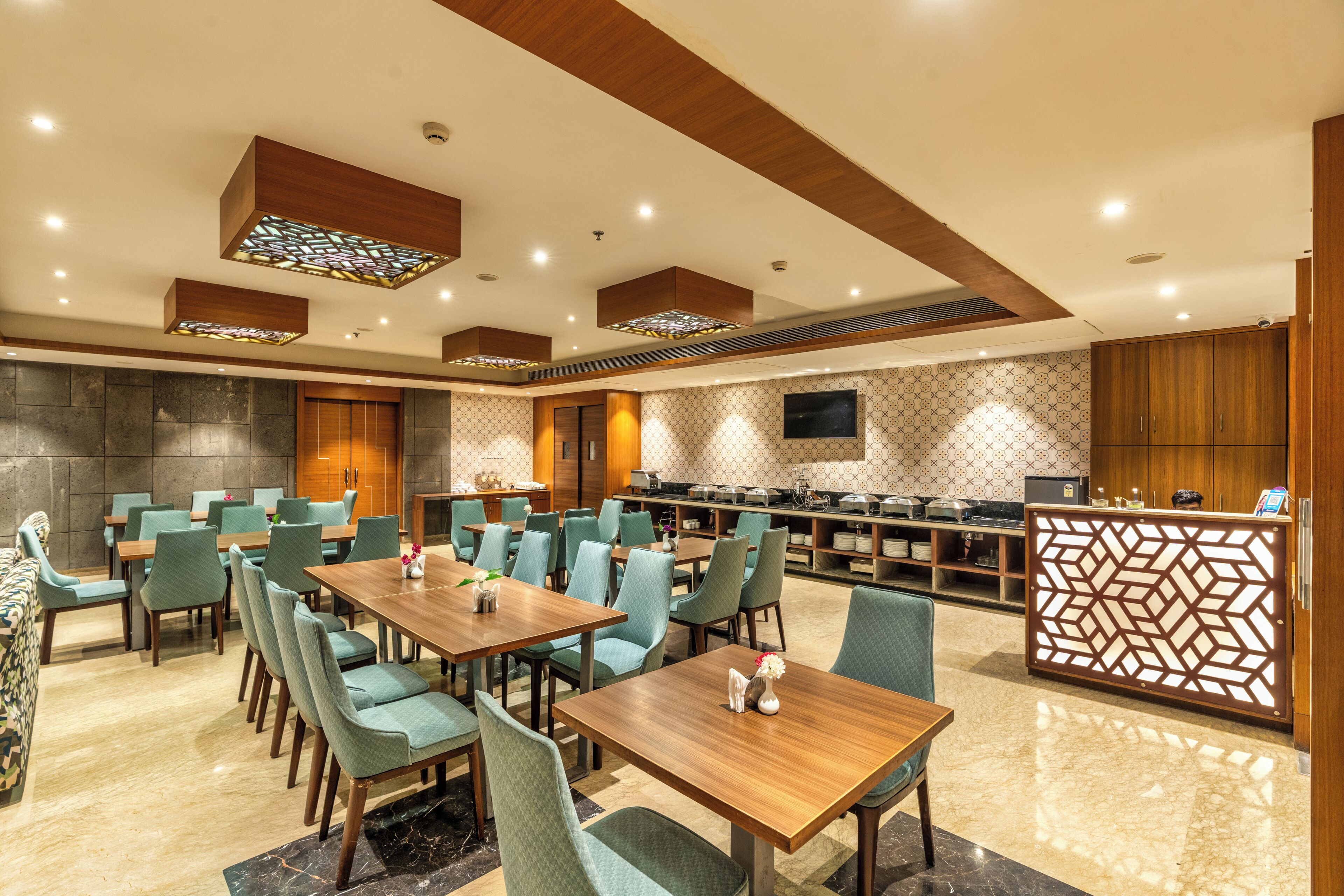 Espaço de refeições de hotel com várias mesas e cadeiras, serviço de buffet e um painel decorativo.