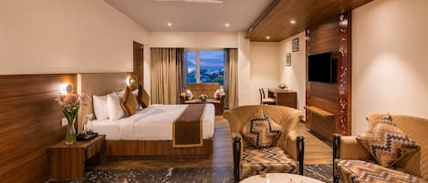 A hotel room with a bed, a sofa, a chair, a small table, and a TV.