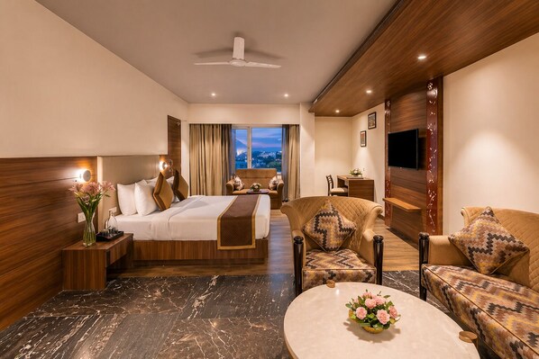 A hotel room with a bed, a sofa, a chair, a small table, and a TV. - Royal Aravali Udaipur (Udaipur)