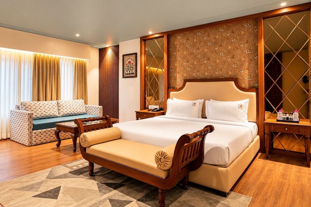 A hotel room with a large bed, a sofa, a wooden side table, and a nightstand.