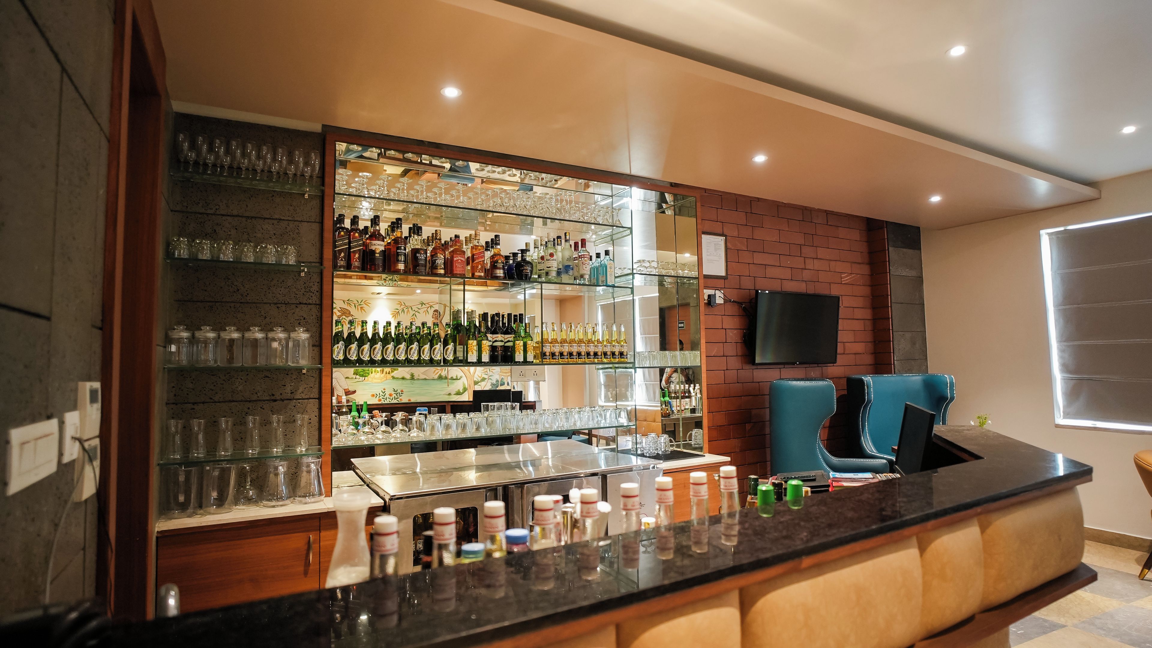 A bar area with a counter, shelves of bottles, glasses, and seating.