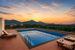 A rooftop swimming pool with lounge chairs and a cityscape view at sunset. - Royal Aravali Udaipur (Udaipur)