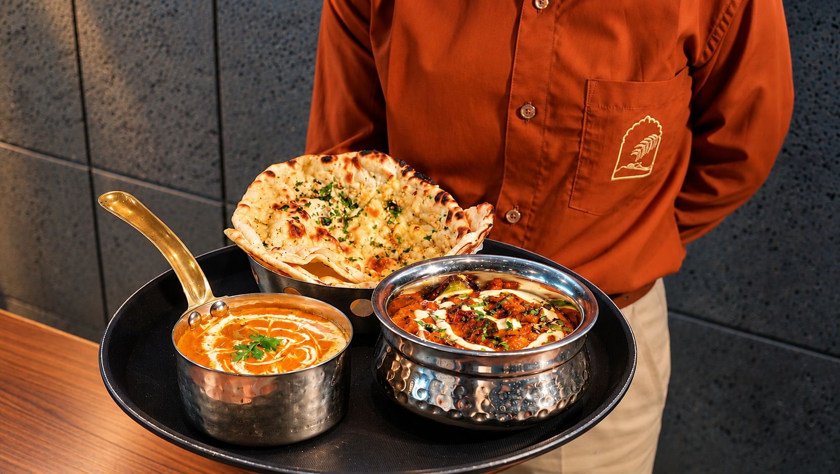 A person serving a meal consisting of naan bread, butter chicken, and butter masala.