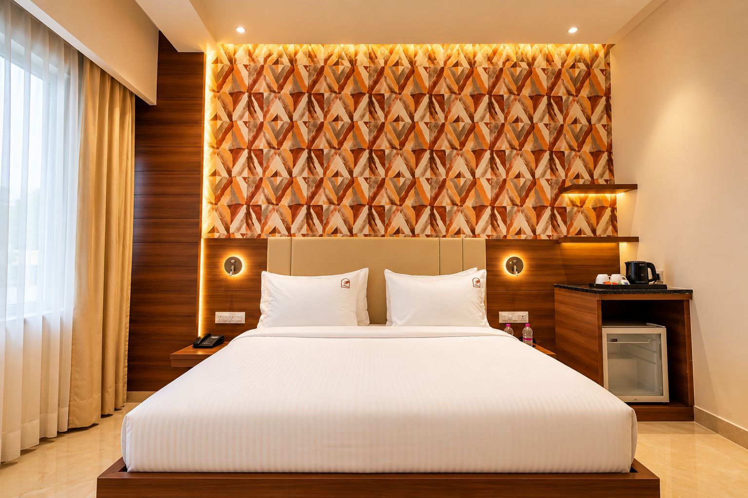 A hotel room with a large bed, a wooden headboard, a wall with a geometric pattern, bedside lamps, a nightstand, a coffee maker, and a mini fridge.