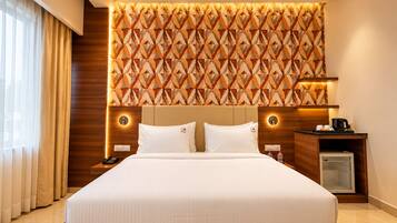 A hotel room with a large bed, a wooden headboard, a wall with a geometric pattern, bedside lamps, a nightstand, a coffee maker, and a mini fridge.