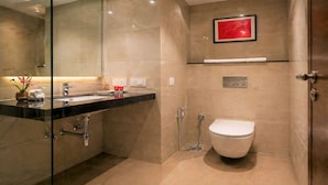 A modern bathroom with a glass-enclosed shower, a white toilet, and a vanity with a black countertop. - Royal Aravali Udaipur (Udaipur)