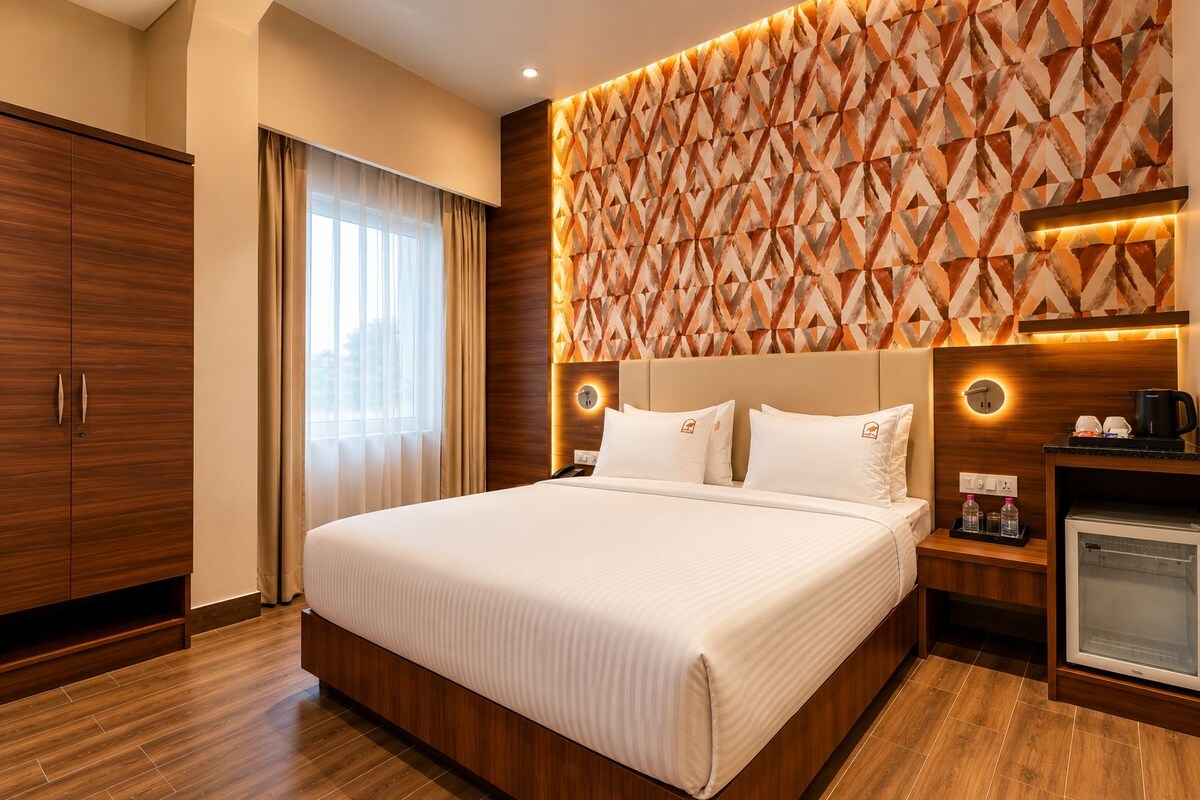 A hotel room with a large bed, wooden wardrobe, a minibar, and a patterned wall.