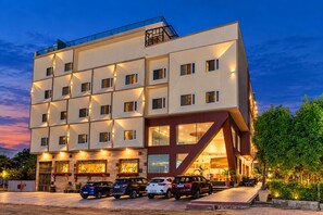 A multi-story hotel with a modern design, featuring a parking area with several cars and a well-maintained garden. - Royal Aravali Udaipur (Udaipur)