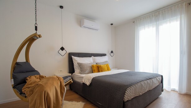 A bedroom with a bed, a hanging chair, a white rug, and a wooden floor. - Modern 2BR Top Floor Apartment + Free Parking (Pula)