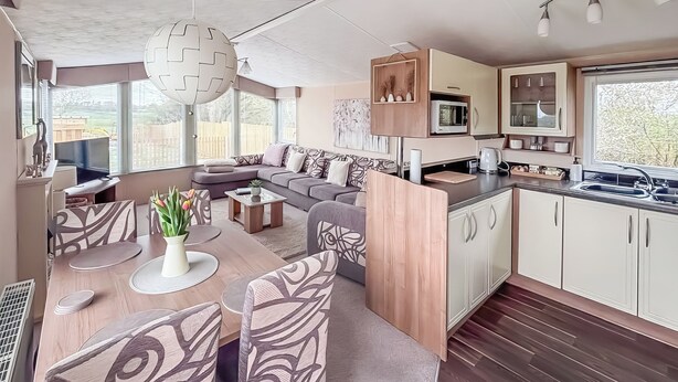 Ein modernes Wohnmobil-Interieur mit Essbereich, Sofa, Küche und großen Fenstern.