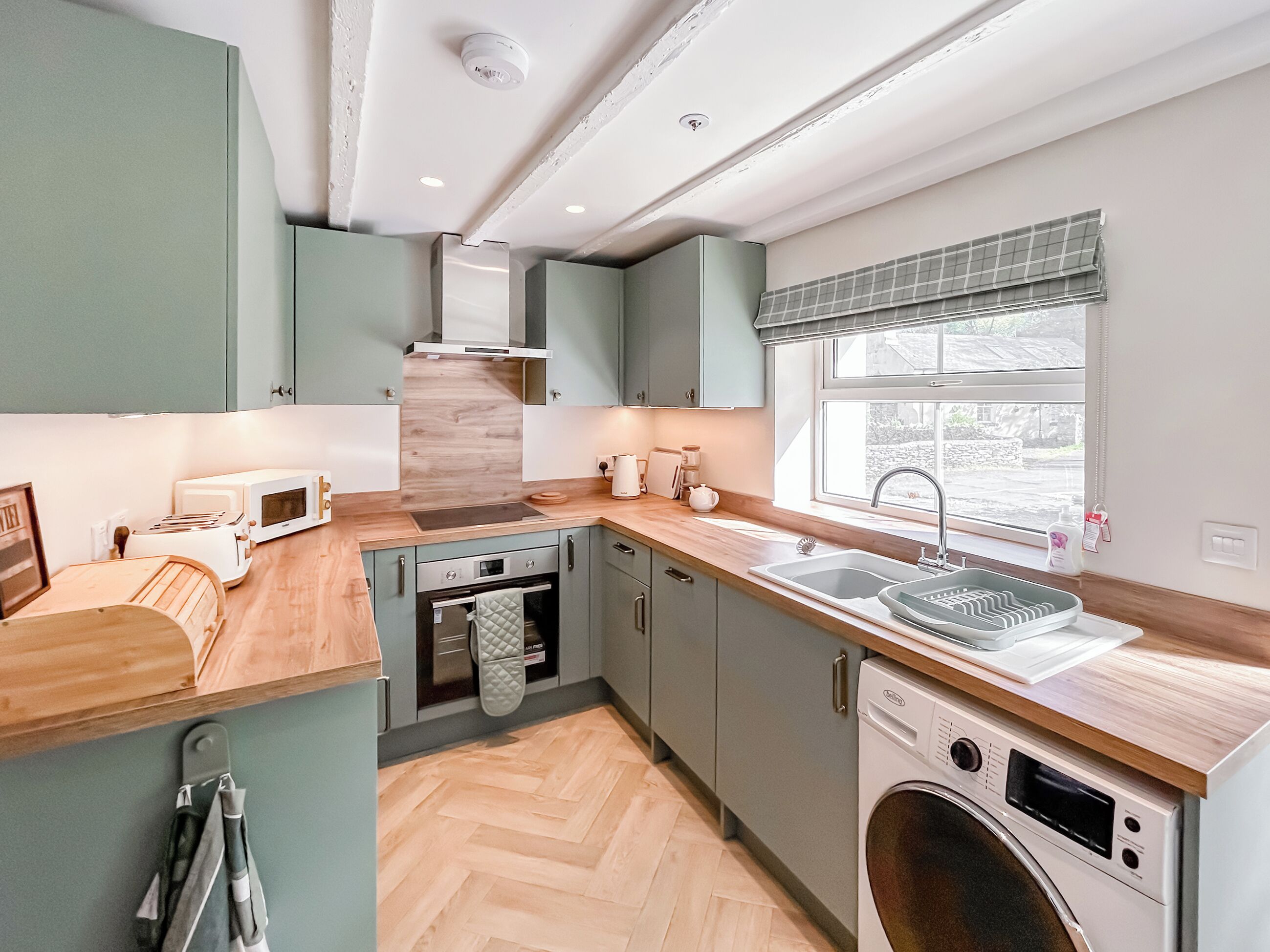 Una cocina compacta con horno integrado, microondas y lavavajillas, encimeras de madera y una ventana con vistas.