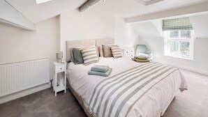 A bedroom with a large bed, a nightstand, a chair, a window with blinds, and a skylight. - 2 bedroom accommodation in Church Hill, Laxey (Church Hill, Laxey)