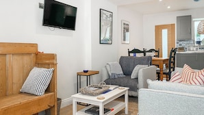A living room with a wooden bench, a grey sofa, a white coffee table, and a television mounted on the wall.