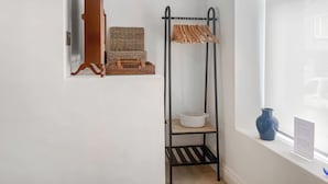 A corner room with a black metal shelf, a wicker basket, a white wicker chair, and a blue vase by the window.