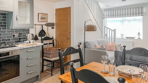 A modern kitchen with a dining area, featuring a wooden table set for two, a built-in oven, and a staircase leading to another level.