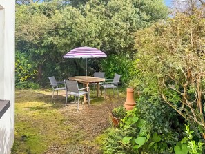 Eine Terrasse mit Tisch, Stühlen, einem Sonnenschirm und Topfpflanzen.
