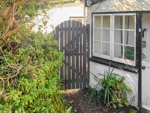 A garden with a black gate, a white building with a window, and greenery.