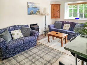 Ein Wohnzimmer mit zwei gemusterten Sofas, einem Holztisch, einer Lampe, einem Gemälde und einem Fenster mit Blick auf Grünfläche.
