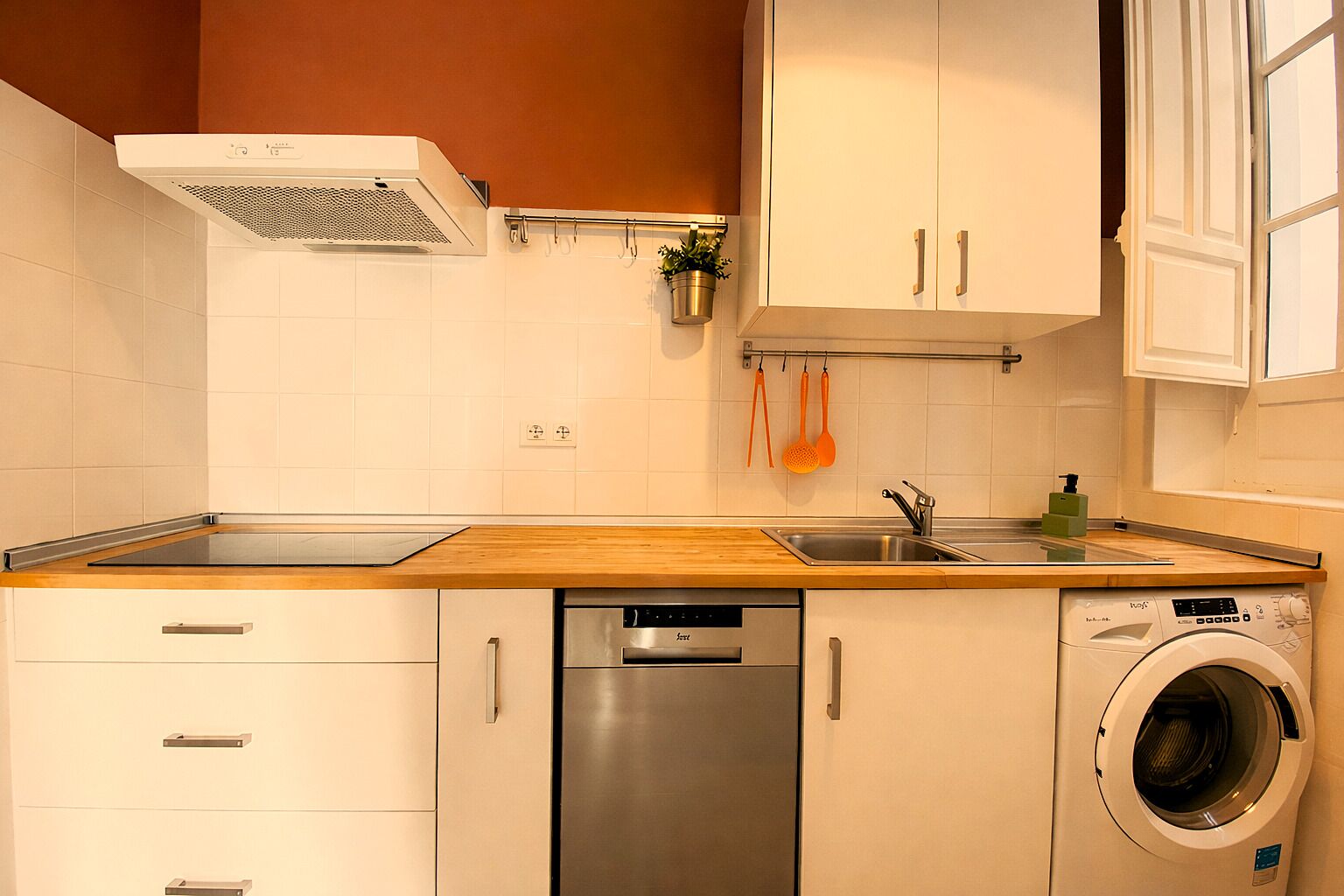 Een keuken met een vaatwasser, wasmachine en een houten aanrecht.