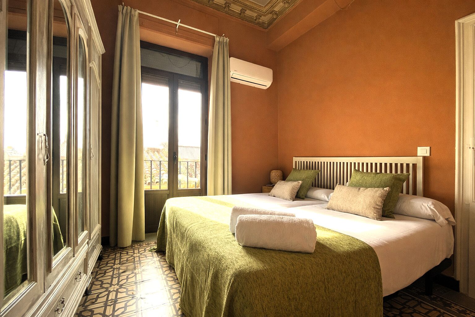 A hotel room with a large bed, a window with curtains, an air conditioning unit, and a balcony view.