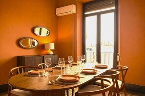 Uma área de jantar com uma mesa posta para seis pessoas, um ar condicionado fixado na parede e uma grande janela com vista.