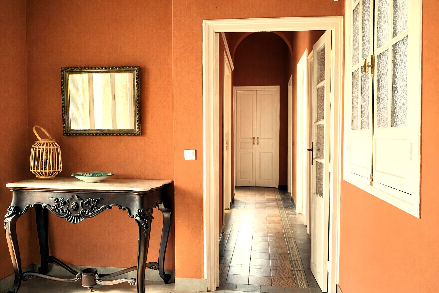 A hallway with a table and a framed picture on the wall, leading to a door with a patterned window.