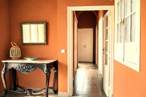 Um corredor com uma mesa e um quadro pendurado na parede, que leva a uma porta com vitrais.