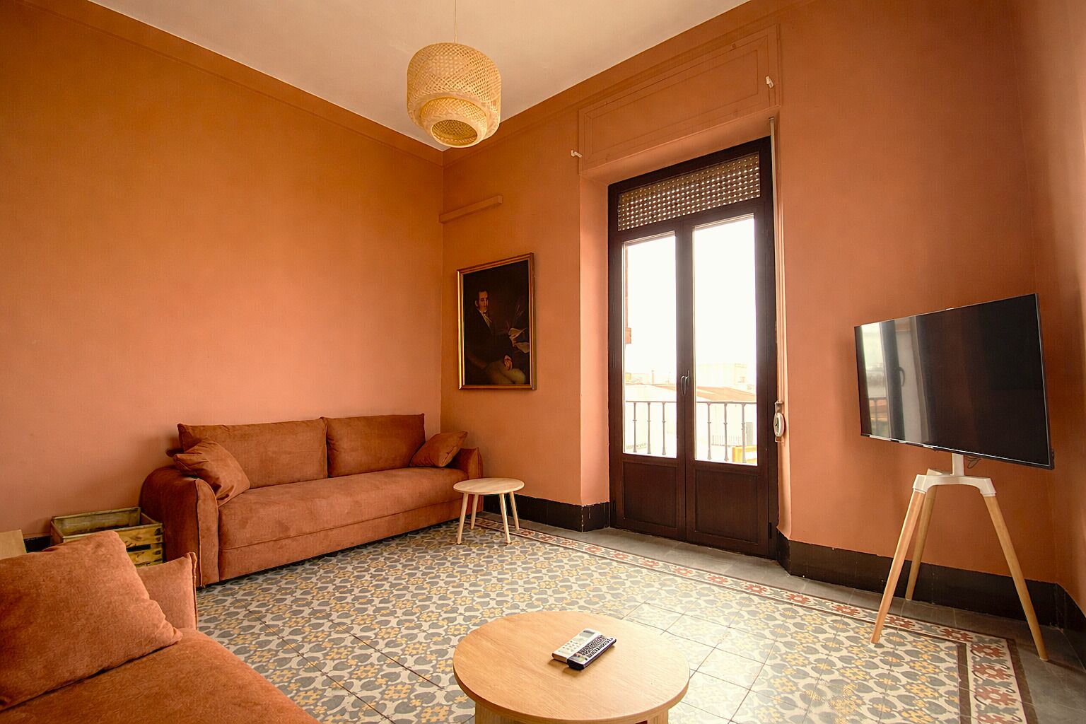 Een kamer met een bank, een kleine tafel, een televisie op een standaard, een deur met een raam en een schilderij aan de muur.