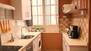 Cocina compacta con lavavajillas integrado, cocina y cafetera.
