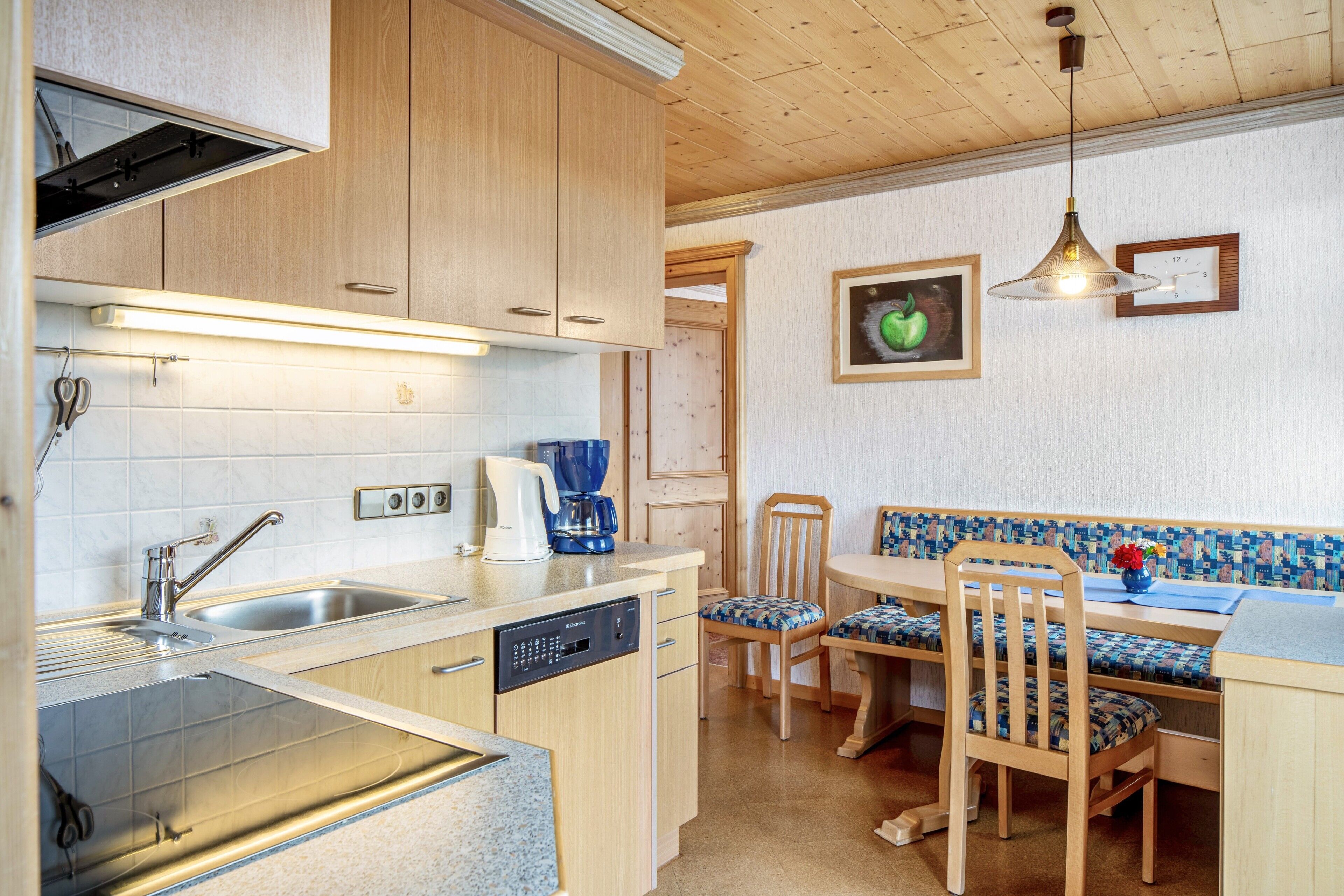 A kitchen with a dishwasher, a coffee maker, and a sink. There is a dining area with a table and chairs.
