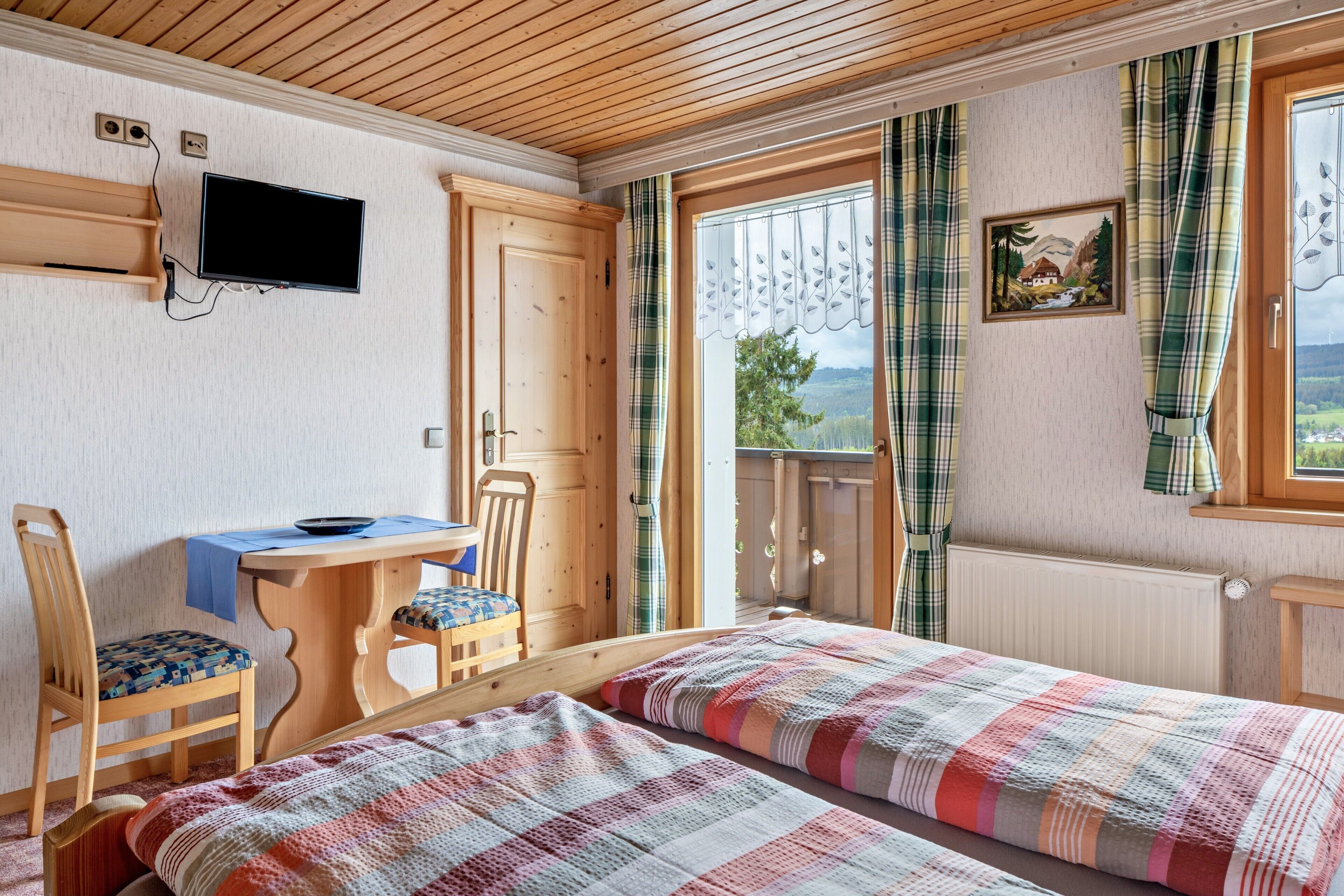 Ein Zimmer mit zwei Betten, einem Schreibtisch, einem Stuhl, einem Fernseher und einem fenster mit Vorhängen.