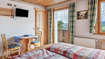 Ein Zimmer mit zwei Betten, einem Schreibtisch, einem Stuhl, einem Fernseher und einem fenster mit Vorhängen.