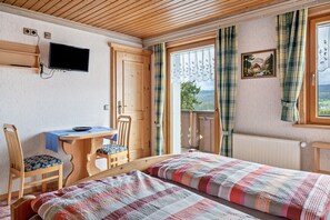 Ein Zimmer mit zwei Betten, einem Schreibtisch, einem Stuhl, einem Fernseher und einem fenster mit Vorhängen.
