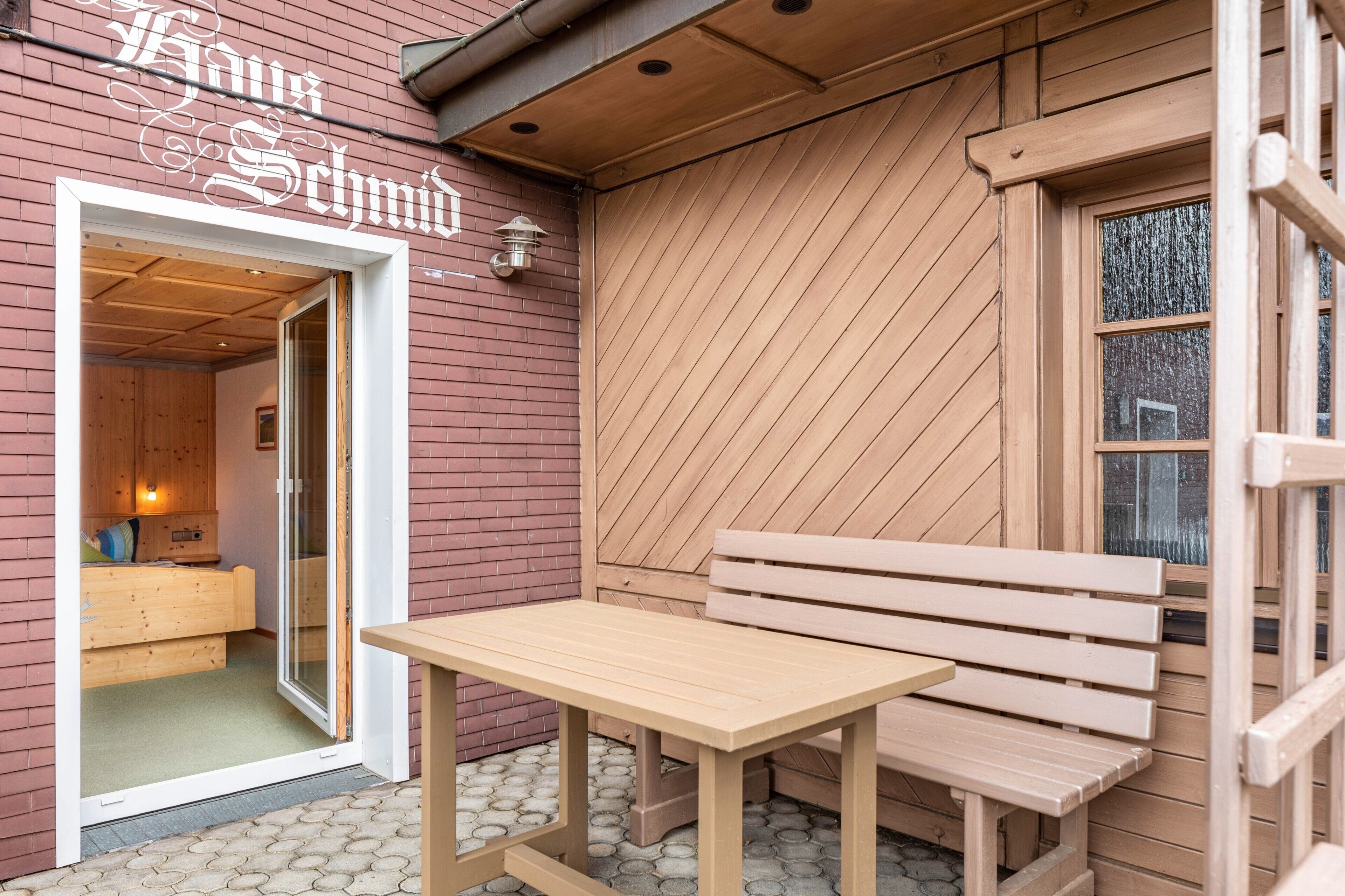 Ein Holzenes Gebäude mit einer Bank und einem Tisch, eine Tür, die zu einem Zimmer mit einem Bett führt, und ein Schild über der Tür.