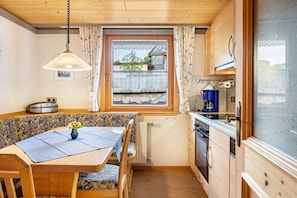 Eine kompakte Küche mit Holzschränken, einem Esstisch mit Stühlen, einem Fenster mit Vorhängen und einer Heizung.