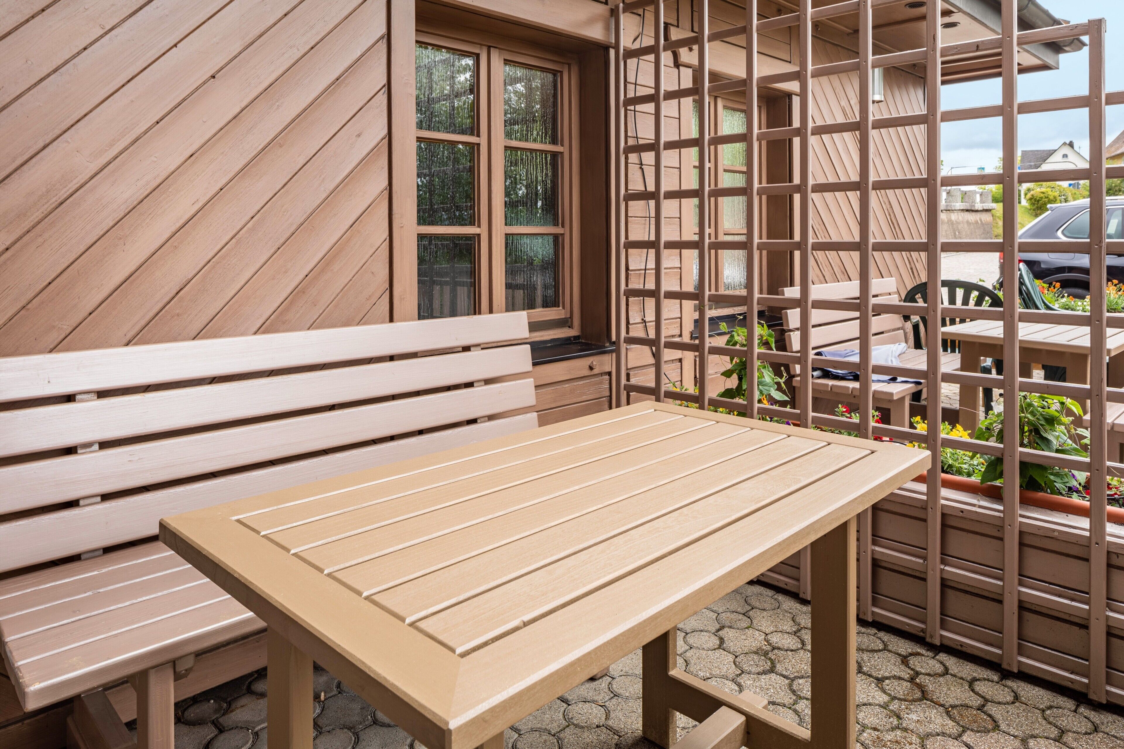 A wooden outdoor seating area with a bench and table, surrounded by a wooden fence and potted plants.