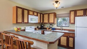 Una cocina con armarios de madera, una estufa blanca, un microondas, un refrigerador y una ventana con vista a palmeras.