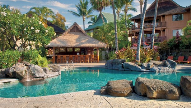 Un resort con piscina, un bar con techo de paja y un edificio de varios pisos con balcones.