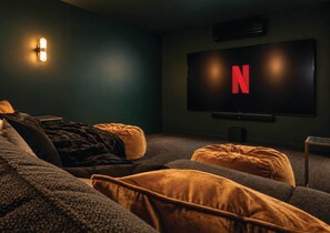 A cozy room with a large flat-screen TV displaying the Netflix logo, a comfortable couch, and a small table. - Kindred Whitsundays (5brm) (Woodwark)
