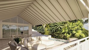 A covered outdoor seating area with a white ceiling, a white sofa, and a large window overlooking a lush garden. - Kindred Whitsundays (5brm) (Woodwark)