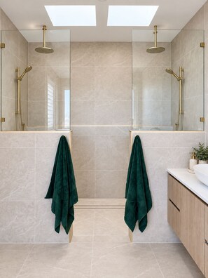 A modern bathroom with two sinks, a large mirror, and a shower with a gold showerhead. - Kindred Whitsundays (5brm) (Woodwark)