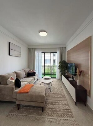 Una sala de estar moderna con sofá, reposapiés, mesa de centro, televisor y un balcón con cortinas.
