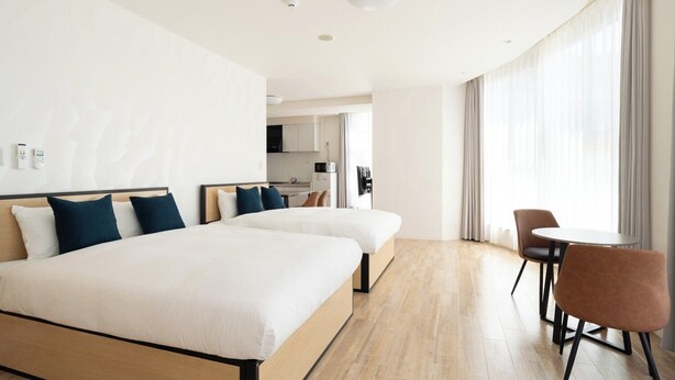 Ein Hotelzimmer mit zwei Betten, einem Essbereich und einer Küche im Hintergrund.
