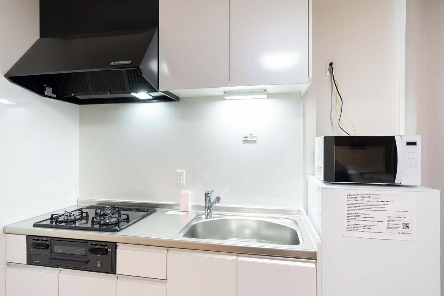 Una cocina con estufa a gas, fregadero y microondas sobre un mueble blanco.