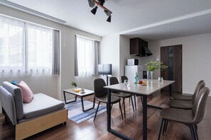 A modern hotel room with a sofa, dining table, chairs, a TV, a microwave, and a plant. - LaSante UMEDAKITA (Osaka)