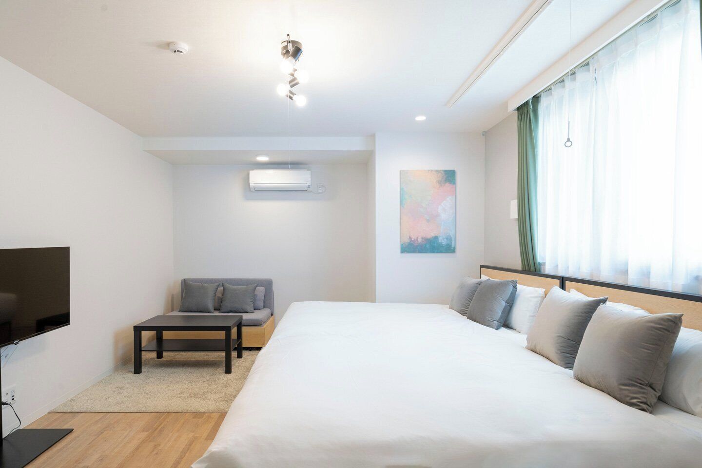 A hotel room with a bed, a TV, a sofa, and a painting.