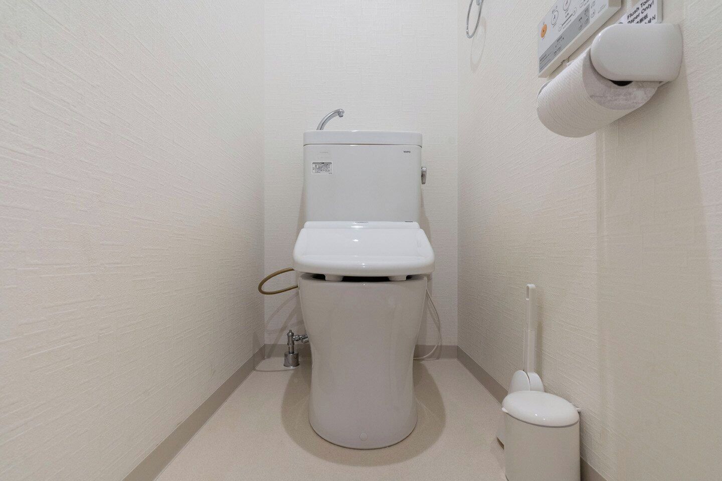 A small, white bathroom with a toilet, a bidet, and a toilet paper holder on the wall.
