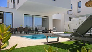 Un área de piscina moderna al aire libre con sillones de descanso, un conjunto de comedor y un césped bien cuidado.