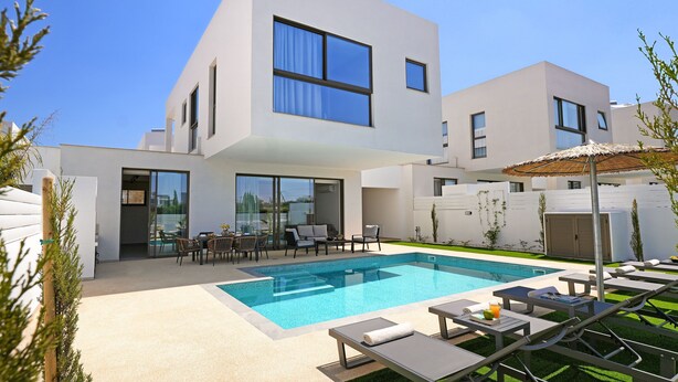 Una casa moderna de dos pisos con piscina, mobiliario exterior y zona de patio.